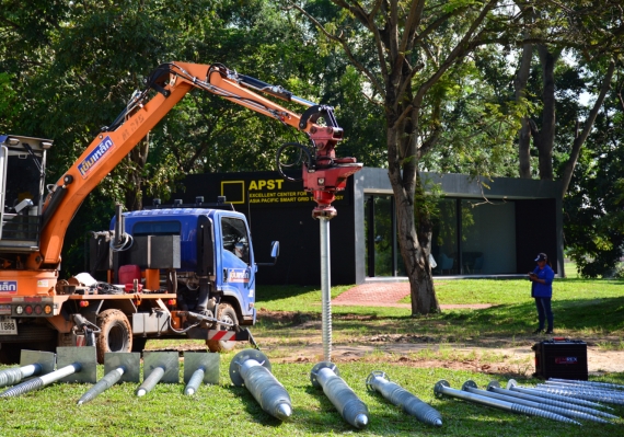 เข็มเหล็ก คือระบบฐานรากสมัยใหม่ที่ใช้เสาเข็มทำจากเหล็กกล้าแทนคอนกรีต มีลักษณะเป็นเสาเหล็กหน้าตัดกลมหรือแบบ H-Beam ที่สามารถตอกหรือติดตั้งลงดินได้โดยตรงเพื่อรองรับโครงสร้างด้านบน แนวคิดนี้ถือเป็นนวัตกรรมในประเทศไทยที่ช่วยให้งานติดตั้งฐานรากรวดเร็วขึ้น ไม่ต้องขุดหลุมขนาดใหญ่หรือรอคอนกรีตเซ็ตตัว โดยเสาเข็มเหล็กมักนิยมใช้ในพื้นที่ดินอ่อน พื้นที่ใกล้แหล่งน้ำ หรือในงานที่ต้องการความรวดเร็วในการติดตั้ง เช่น ฐานรากเสาไฟพลังงานแสงอาทิตย์ ป้ายขนาดใหญ่ หรือโครงสร้างเบาชั่วคราวต่าง ๆ เข็มเหล็กสามารถติดตั้งได้สะดวกในพื้นที่จำกัด ด้วยเครื่องจักรตอกหรือระบบเจาะสกรูลงดิน และสามารถถอดถอนเคลื่อนย้ายได้ง่ายเมื่อหมดอายุการใช้งาน ข้อดี: เข็มเหล็กโดดเด่นเรื่องความรวดเร็วในการทำงาน – สามารถติดตั้งฐานรากแล้วดำเนินการขึ้นโครงสร้างต่อได้ทันทีโดยไม่ต้องรอให้คอนกรีตแข็งตัว นอกจากนี้ยังรองรับน้ำหนักได้ดีในชั้นดินอ่อนหรือพื้นที่ใกล้น้ำ เนื่องจากเสาเหล็กมีความยืดหยุ่นและแรงต้านทานต่อการโก่งตัวสูง อีกทั้งงานติดตั้งค่อนข้างสะอาดและลดขั้นตอนหลายอย่างเมื่อเทียบกับการทำฐานรากคอนกรีต (ไม่ต้องเทปูนหรือทำแบบหล่อหน้างาน) ข้อจำกัด: เนื่องจากวัสดุเป็นเหล็ก การกัดกร่อนจึงเป็นปัจจัยสำคัญที่ต้องคำนึงถึง หากติดตั้งเข็มเหล็กในดินที่มีความชื้นสูงหรือดินเค็ม ต้องมีการป้องกันสนิมที่ดี (เช่น การชุบกัลวาไนซ์หรือทาสีเคลือบป้องกัน) เพื่อยืดอายุการใช้งานของฐานรากเหล็ก นอกจากนี้ราคาเข็มเหล็กอาจสูงกว่าระบบเสาเข็มคอนกรีตขึ้นอยู่กับขนาดและประเภทของเหล็กที่ใช้ แต่เมื่อพิจารณาประหยัดเวลาการติดตั้งและความสะดวก เข็มเหล็กก็เป็นทางเลือกที่คุ้มค่าในหลายกรณี ซึ่งได้รับการยอมรับอย่างแพร่หลายในงานติดตั้งฐานรากยุคใหม่ ถือเป็นการต่อยอดนวัตกรรมฐานรากที่ตอบโจทย์งานโครงสร้างเบาและงานติดตั้งเสาไฟฟ้ากลางแจ้งในประเทศไทย